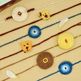 Dhavala, Teddy Bear, Teddy Bear with Bow, Swastika, Sun, Maati and Neel Nazar Battu Eco-friendly Seed Rakhi (Set of 7)
